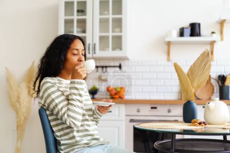Téléchargez les photos : "Femme afro-américaine buvant une tasse de thé et appréciant le matin. Concept de style de vie lent" - en image libre de droit