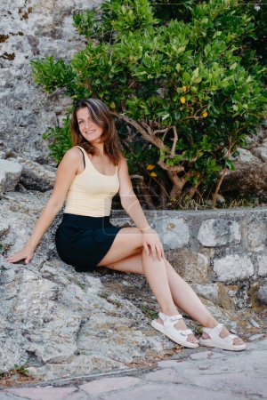 Téléchargez les photos : Belle fille est assise sur le mur de pierre de la vieille ville de Budva. La fille est assise sur un parapet en pierre, Budva, Monténégro - en image libre de droit