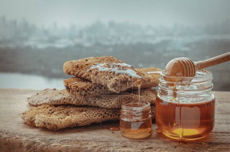 Foto de "Deliciosa miel goteando de panales frescos en tarro de vidrio con palo de madera de la cacerola de miel en la vieja mesa de madera. " - Imagen libre de derechos
