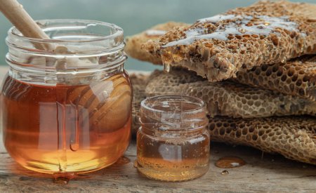 Photo for "Close-up of Delicious honey dripping from Fresh honeycombs on Glass jar with Wooden honey dipper stick on old wooden table. " - Royalty Free Image