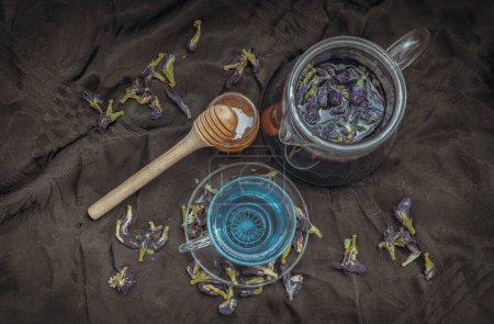 Photo for "Butterfly pea tea (Clitoria) or Organic blue anchan in Teapot and glass cup served with honey on Dark background. " - Royalty Free Image
