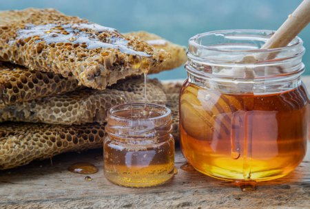 Foto de "Primer plano de la miel deliciosa goteando de panales frescos en tarro de vidrio con palo de madera de la cacerola de miel en la mesa de madera vieja. " - Imagen libre de derechos