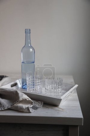 Foto de "Una botella de agua azul transparente y dos vasos acanalados en una bandeja de madera blanca en la mesa de la cocina." - Imagen libre de derechos