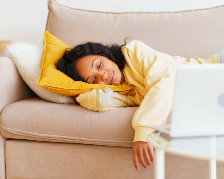 Téléchargez les photos : "Heureuse et souriante femme afro-américaine couchée sur le canapé et regardant des films sur ordinateur portable" - en image libre de droit