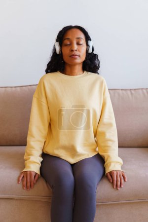 Téléchargez les photos : "Femme afro-américaine assise sur un canapé et écoutant de la musique dans un casque. Thérapie respiratoire" - en image libre de droit