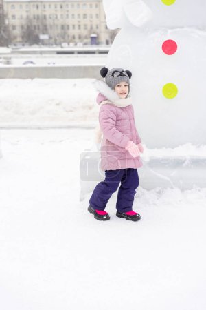 Téléchargez les photos : Enfant ludique fille heureux dans la ville enneigée le jour de l'hiver - en image libre de droit