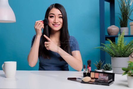 Téléchargez les photos : Asian content creator using brush while doing makeup tutorial at camera - en image libre de droit