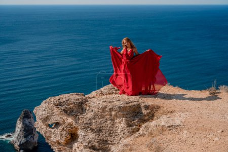Photo for A woman in a red flying dress fluttering in the wind, against the backdrop of the sea. - Royalty Free Image