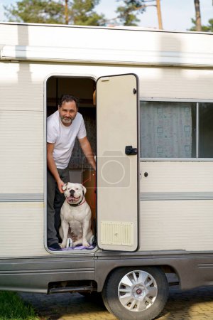 Photo for A man with a cute American Bulldog breed dog travels in a motorhome. - Royalty Free Image