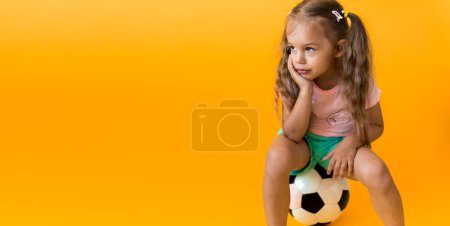 Photo for Authentic cute smiling preschool little girl with classic black and white soccer ball look at camera on yellow background. child play football in t-shirt and shorts. Sport, championship, team concept - Royalty Free Image