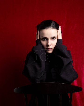 Foto de "una mujer en un suéter negro se sienta en una silla, fondo rojo" - Imagen libre de derechos