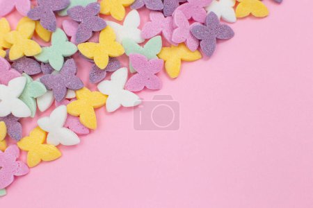 Téléchargez les photos : "Papillons colorés, une garniture de confiserie populaire, reposent sur un fond rose en diagonale dans le coin gauche." - en image libre de droit