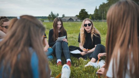 Foto de "Un grupo de estudiantes femeninas están sentadas en un círculo en un prado para el trabajo colectivo con cuadernos." - Imagen libre de derechos
