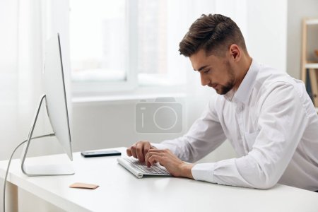 Téléchargez les photos : Bel homme employé de bureau dans une chemise blanche travaillant dans un bureau moderne - en image libre de droit
