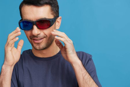 Téléchargez les photos : Homme joyeux dans des lunettes de cinéma dans un t-shirt sur fond bleu - en image libre de droit