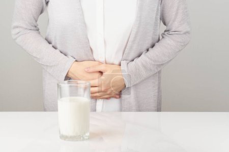Foto de Mujer al lado de un vaso de leche con dolor de estómago - Imagen libre de derechos
