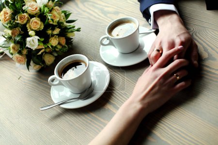 Photo for "Wedding couple holding hands with cups of coffee at wooden table" - Royalty Free Image