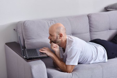 Foto de "Hombre joven en sala de estar con ordenador portátil" - Imagen libre de derechos