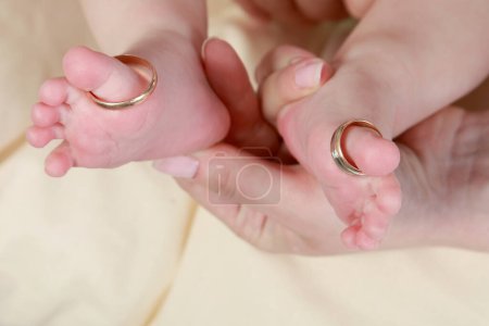 Téléchargez les photos : "pied de bébé dans les mains de la mère avec soin avec des anneaux sur les orteils" - en image libre de droit