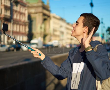 Foto de Joven con un teléfono está en la calle de una gran ciudad y agitando la mano - Imagen libre de derechos