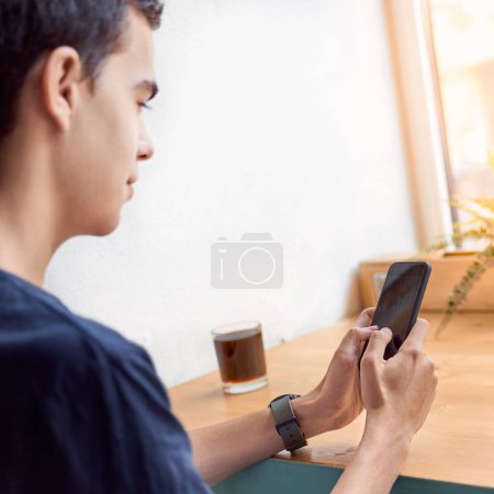 Foto de Adulto joven mirando el teléfono móvil, sentado en la cafetería. Era digital. La gente se comunica en chat. - Imagen libre de derechos