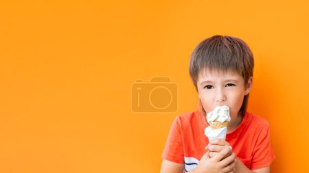 Foto de El niño come helado al aire libre. Niño en monocromo, fondo de pared naranja brillante. Sabroso postre frío en verano. - Imagen libre de derechos