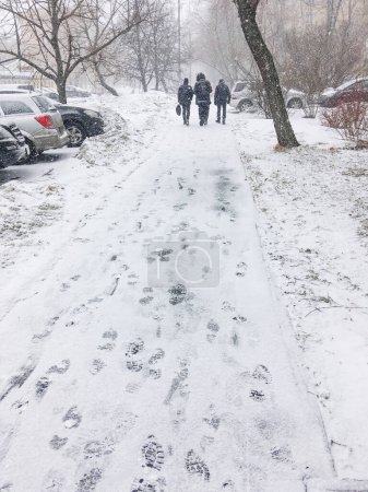 Photo for Three men walk down the street covered with snow. Footprints on snowy pavement. Winter in town. - Royalty Free Image