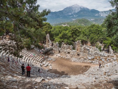 Foto de "PHASELIS, TURQUÍA - 19 de mayo de 2018. Los turistas caminan en ruinas del anfiteatro de la antigua ciudad de Phaselis. Vista panorámica del famoso monumento arquitectónico, distrito de Kemer, provincia de Antalya
." - Imagen libre de derechos