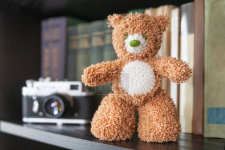 Photo for "Hand made teddy bear on bookshelf. Crocheted brown toy for children. Cute souvenir, handicraft product." - Royalty Free Image