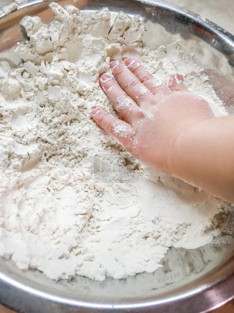 Téléchargez les photos : "Le petit enfant touche la farine dans un bol en métal. Cuisiner avec des enfants. Développer la motricité fine en laissant toucher les ingrédients alimentaires." - en image libre de droit