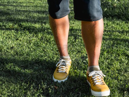 Photo for Man in bright yellow sneakers is standing on green grass lawn in park. Modern hipster's shoes. Urban fashion. - Royalty Free Image