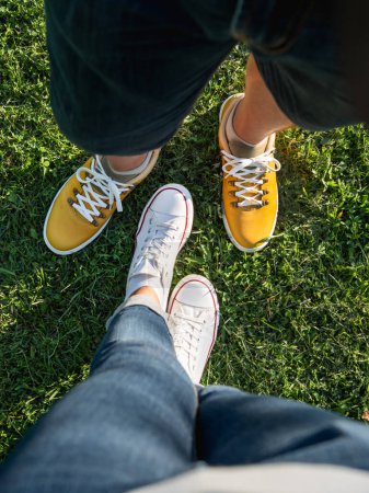 Photo for Man and woman stand on green grass lawn in park. Couple on date. Upper view on modern hipster's sneakers. Urban fashion. - Royalty Free Image