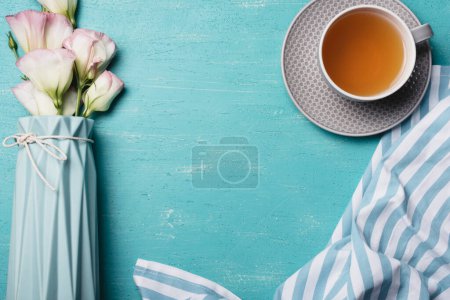 Foto de Florero eustoma con taza de té servilleta fondo azul - Imagen libre de derechos