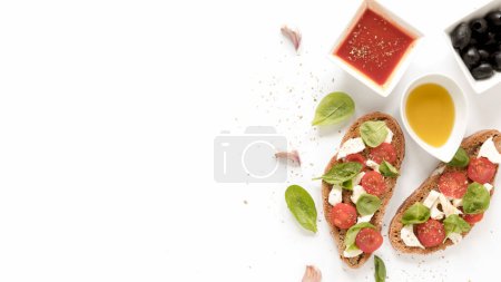 Foto de Bruschetta con queso hojas de albahaca de tomate cubierta cerca de la salsa aceitunas aceite diente de ajo superficie blanca - Imagen libre de derechos