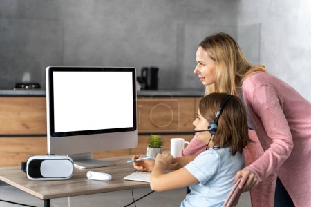Photo for Girl with headset learning online with mother by her side - Royalty Free Image
