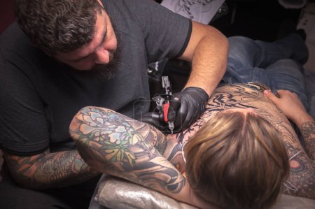 Téléchargez les photos : "Tatoueur démontre le processus de se faire tatouer en studio de tatouage" - en image libre de droit