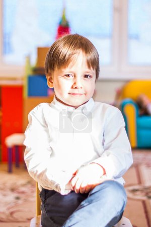Téléchargez les photos : "Elegantly dressed in a white shirt, a little boy is sitting in the classroom for lessons. portrait of a boy" - en image libre de droit