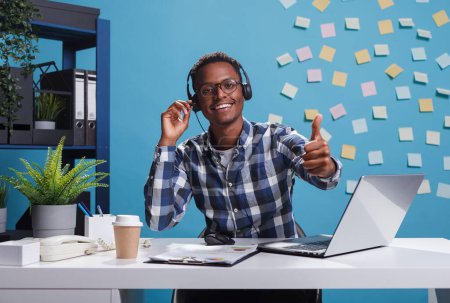 Photo for "Cheerful smiling african american helpline center operator wearing headset, showing thumbs up" - Royalty Free Image