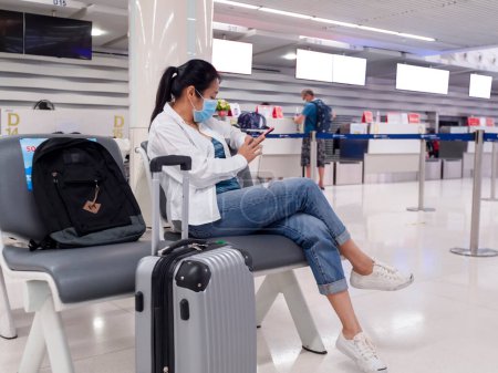 Foto de Asiático viajero mujeres usar mascarillas sentado social distanciamiento sillas de corona virus pandemia en el aeropuerto. - Imagen libre de derechos