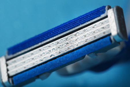 Téléchargez les photos : "Shaving machine with three blades on a blue background with water drops in close-up" - en image libre de droit