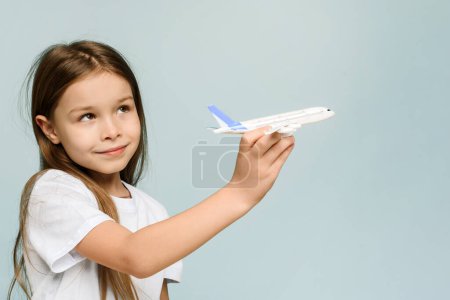Téléchargez les photos : "Fille heureuse jouant avec un avion jouet sur un fond bleu. Voyages en famille et tourisme, concept de vacances d'été." - en image libre de droit