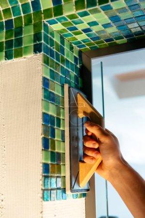 Photo for "Worker applying mosaic tiles in bathroom walls" - Royalty Free Image