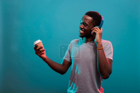 Téléchargez les photos : "Carefree person enjoying mp3 music on headphones and cup of coffee" - en image libre de droit