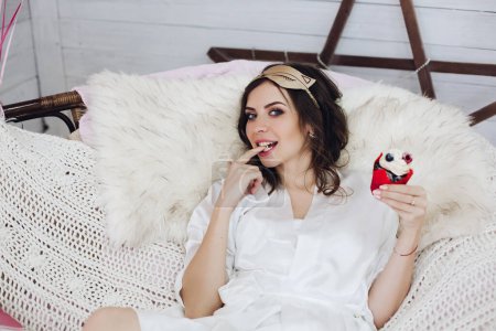 Foto de "Bonita novia en bata blanca y máscara para dormir con pastel de bayas en el sofá." - Imagen libre de derechos