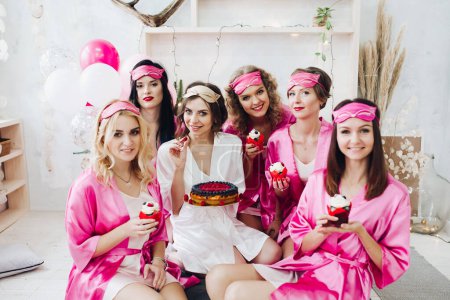 Photo for "Pretty girls in pink robes and sleep masks with desserts at bridal showers." - Royalty Free Image