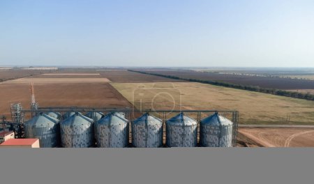 Photo for "Grain elevator. Metal grain elevator in agricultural zone. Agriculture storage for harvest. Grain elevators on green nature background. Exterior of agricultural factory. Nobody." - Royalty Free Image