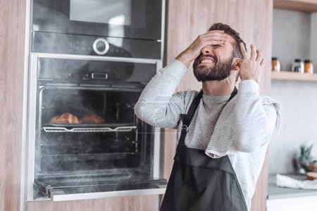 Photo for "surprised man standing near the oven with burnt croissants." - Royalty Free Image