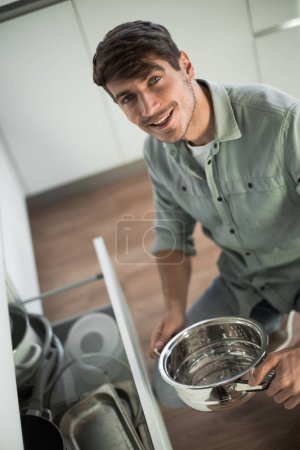 Téléchargez les photos : "jeune homme regardant la vaisselle propre au lave-vaisselle" - en image libre de droit