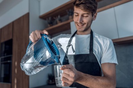 Photo for "young man pours clean water into a glass" - Royalty Free Image
