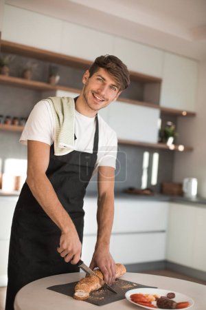 Photo for "smiling man in an apron, slicing the bread for sandwiches" - Royalty Free Image